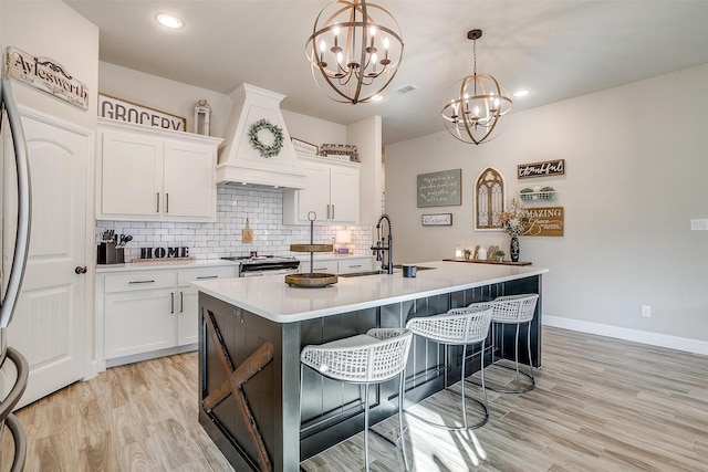 kitchen featuring premium range hood, white cabinetry, stainless steel range, a kitchen island with sink, and hanging light fixtures