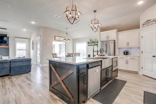 kitchen featuring pendant lighting, white cabinetry, stainless steel appliances, an island with sink, and vaulted ceiling