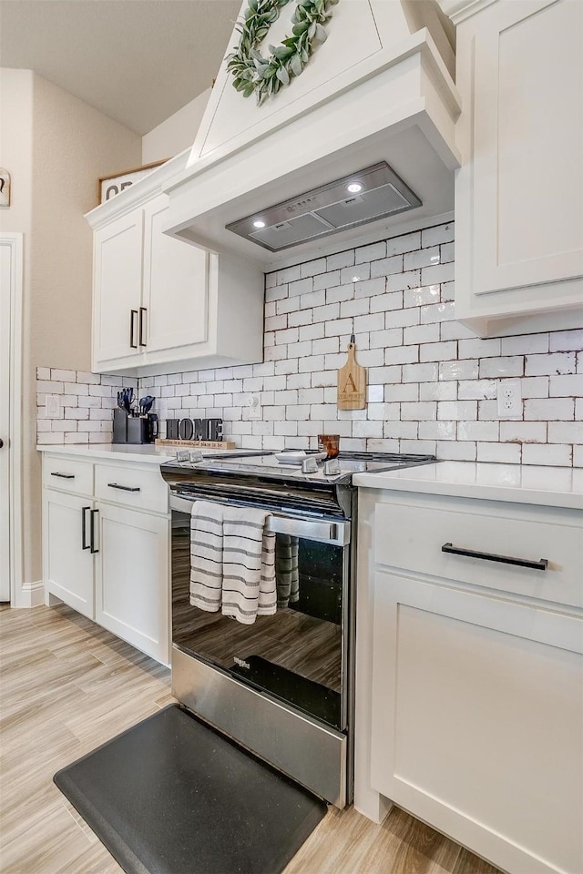 kitchen with electric stove, white cabinetry, premium range hood, and tasteful backsplash