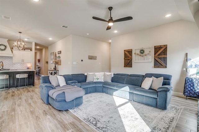 living room with lofted ceiling, ceiling fan with notable chandelier, and light hardwood / wood-style flooring