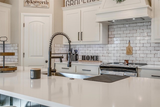 kitchen with white cabinetry, decorative backsplash, premium range hood, stainless steel stove, and sink