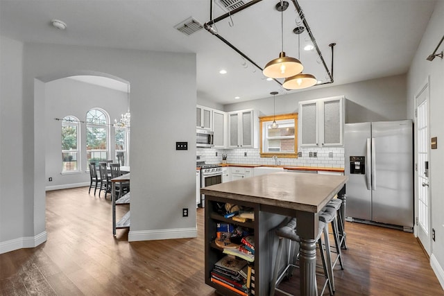 kitchen with appliances with stainless steel finishes, decorative light fixtures, white cabinets, tasteful backsplash, and a center island