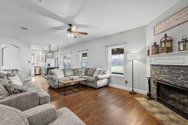 living room with wood-type flooring, ceiling fan, and a stone fireplace