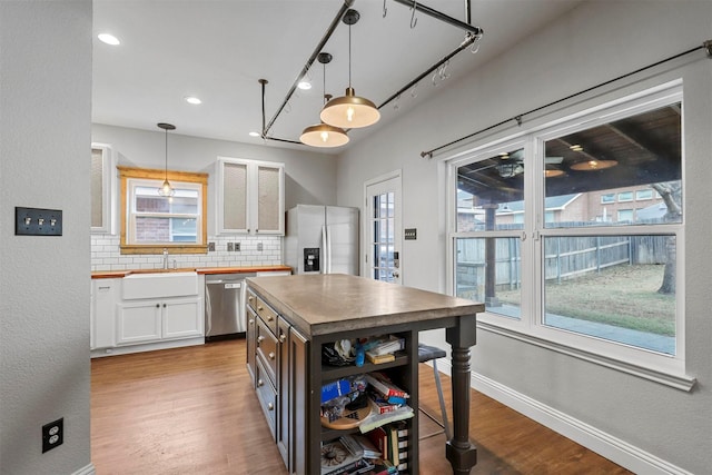 kitchen featuring appliances with stainless steel finishes, decorative light fixtures, white cabinetry, tasteful backsplash, and sink