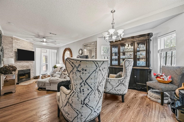 interior space featuring crown molding, a stone fireplace, hardwood / wood-style floors, ceiling fan with notable chandelier, and a textured ceiling