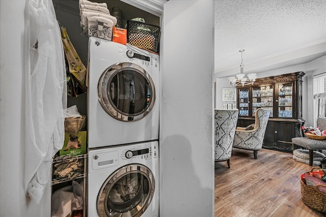 clothes washing area with hardwood / wood-style floors, an inviting chandelier, a healthy amount of sunlight, and stacked washer / drying machine