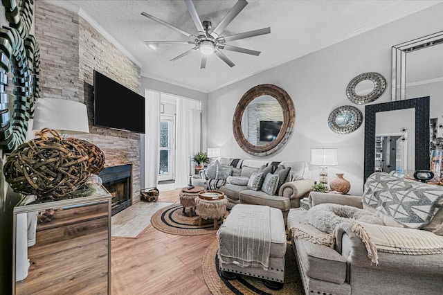 living room with light hardwood / wood-style floors, a textured ceiling, a stone fireplace, and ornamental molding