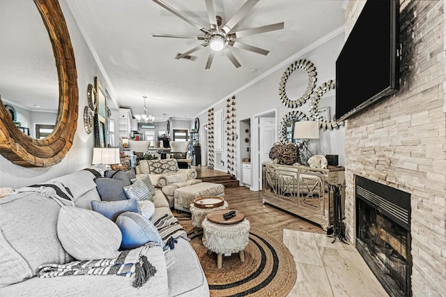 living room featuring light hardwood / wood-style flooring, a stone fireplace, ceiling fan with notable chandelier, a textured ceiling, and ornamental molding