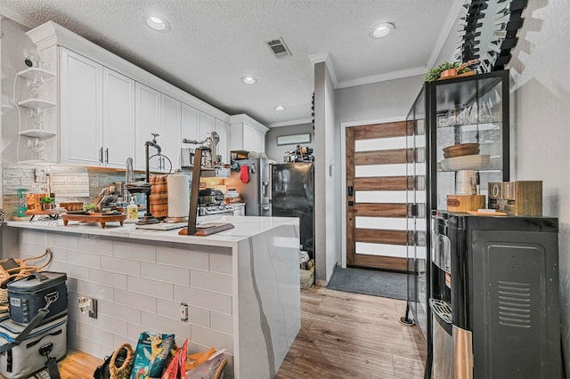 kitchen with a textured ceiling, light hardwood / wood-style floors, white cabinetry, and kitchen peninsula