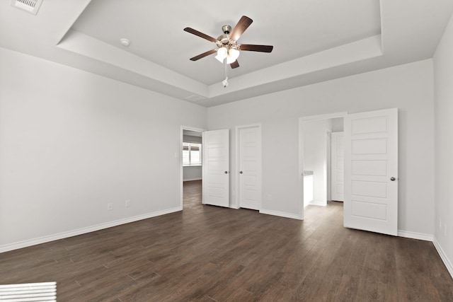 unfurnished bedroom with ceiling fan, a tray ceiling, and dark hardwood / wood-style flooring