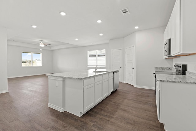 kitchen with appliances with stainless steel finishes, an island with sink, white cabinets, dark hardwood / wood-style flooring, and light stone counters