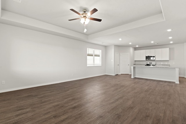 unfurnished living room featuring dark wood-type flooring, a raised ceiling, and ceiling fan