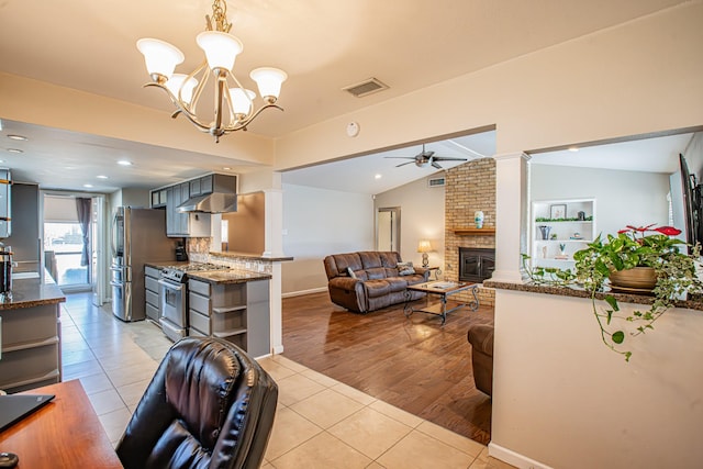 tiled living room featuring ornate columns, a brick fireplace, vaulted ceiling, ceiling fan with notable chandelier, and sink