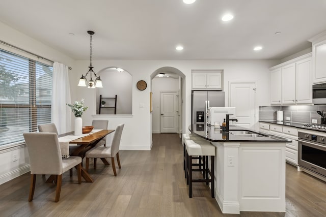 kitchen featuring hardwood / wood-style flooring, an island with sink, appliances with stainless steel finishes, hanging light fixtures, and white cabinets