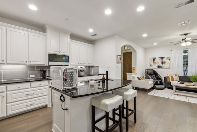 kitchen featuring white cabinets, decorative backsplash, and an island with sink