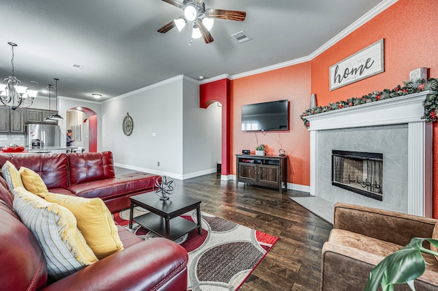 living room featuring a tiled fireplace, dark hardwood / wood-style flooring, ceiling fan with notable chandelier, and ornamental molding