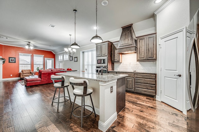 kitchen with light stone countertops, decorative light fixtures, stainless steel appliances, an island with sink, and decorative backsplash