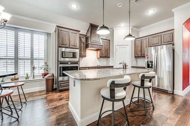 kitchen with pendant lighting, stainless steel appliances, an island with sink, backsplash, and light stone counters