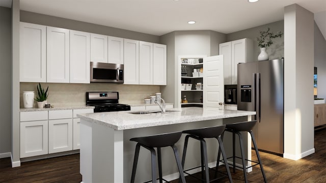 kitchen featuring appliances with stainless steel finishes, white cabinets, a center island with sink, and tasteful backsplash