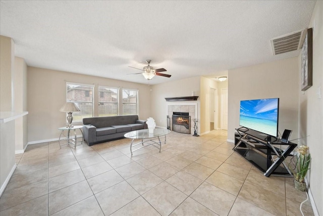 tiled living room with ceiling fan, a tiled fireplace, and a textured ceiling