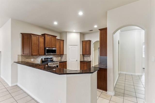 kitchen featuring kitchen peninsula, decorative backsplash, light tile patterned flooring, stainless steel appliances, and dark stone counters