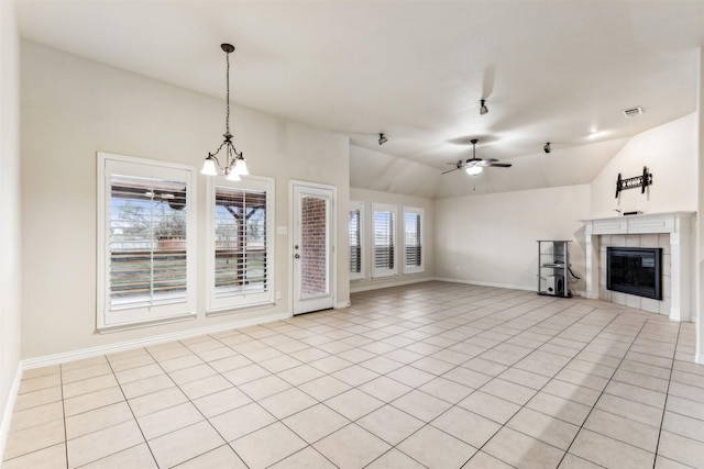 unfurnished living room with ceiling fan with notable chandelier, light tile patterned floors, a tile fireplace, and vaulted ceiling