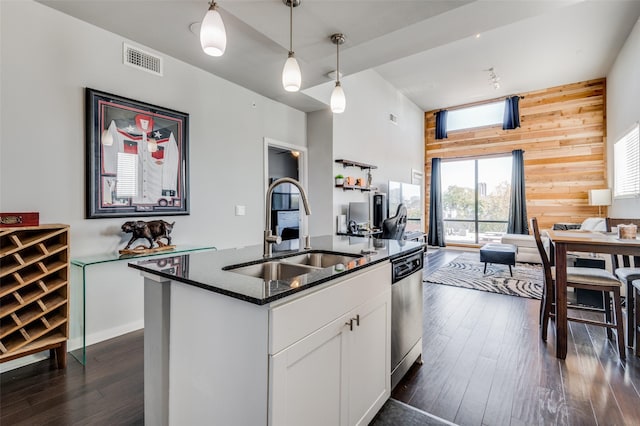 kitchen with wood walls, sink, hanging light fixtures, an island with sink, and white cabinets