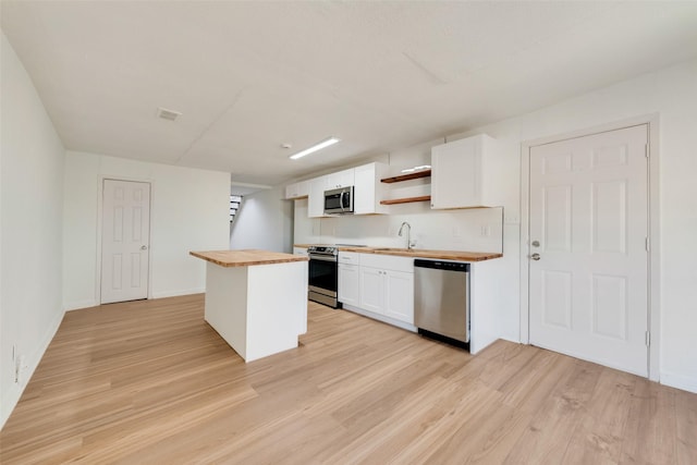 kitchen with white cabinets, butcher block countertops, appliances with stainless steel finishes, and sink