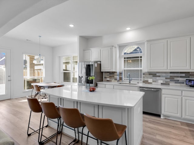 kitchen featuring a center island, appliances with stainless steel finishes, white cabinetry, hanging light fixtures, and sink