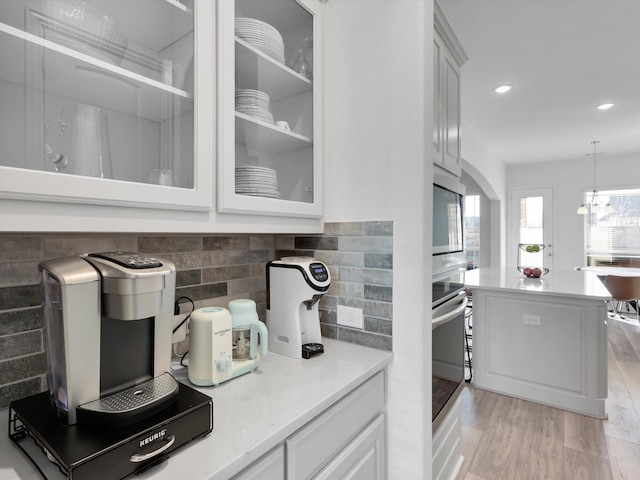 kitchen with stainless steel oven, built in microwave, white cabinetry, hanging light fixtures, and light hardwood / wood-style flooring