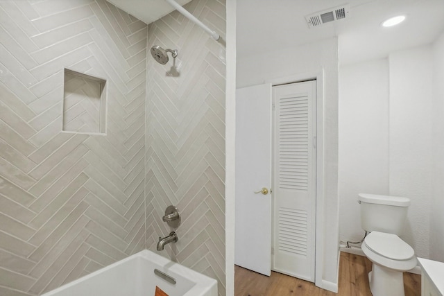 bathroom with wood-type flooring, toilet, and tiled shower / bath