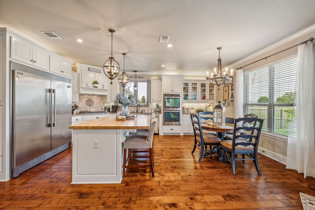 kitchen featuring white cabinets, appliances with stainless steel finishes, a center island, wood counters, and an inviting chandelier