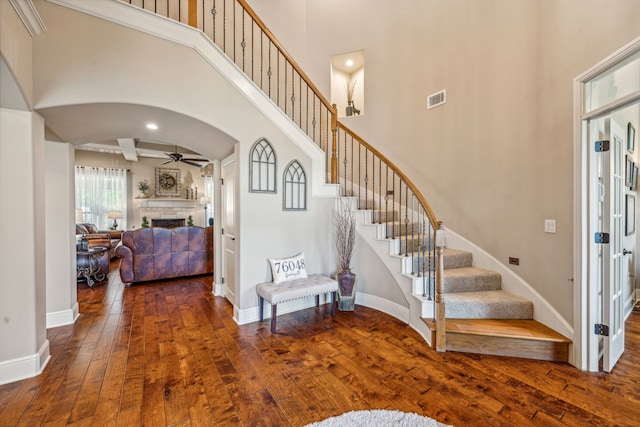 staircase featuring ceiling fan, wood-type flooring, beam ceiling, and a towering ceiling