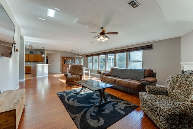 living room with vaulted ceiling, ceiling fan with notable chandelier, and light hardwood / wood-style flooring