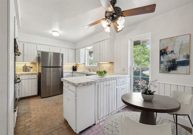 kitchen with kitchen peninsula, stainless steel fridge, backsplash, white cabinets, and sink