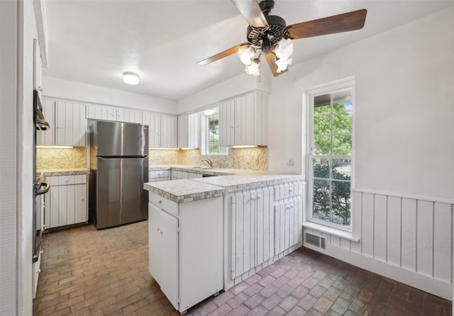 kitchen with kitchen peninsula, stainless steel fridge, backsplash, white cabinets, and sink