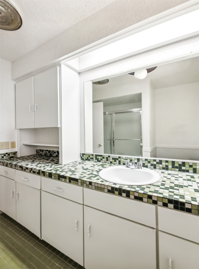 bathroom with vanity, a shower with door, and a textured ceiling