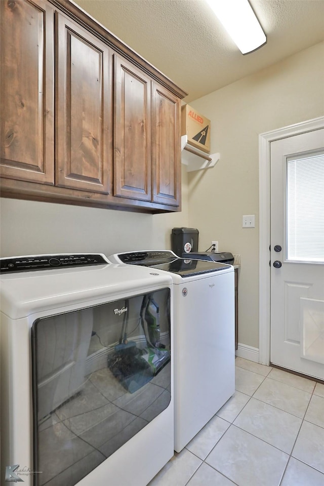 clothes washing area with cabinets, a textured ceiling, light tile patterned floors, and independent washer and dryer