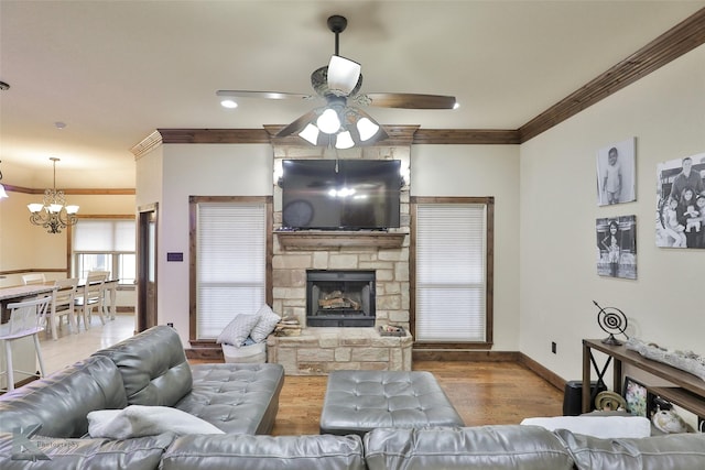 living room with ceiling fan with notable chandelier, a stone fireplace, ornamental molding, and light hardwood / wood-style flooring