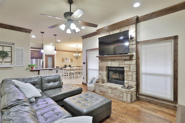 living room with a fireplace, ornamental molding, ceiling fan with notable chandelier, and light hardwood / wood-style flooring