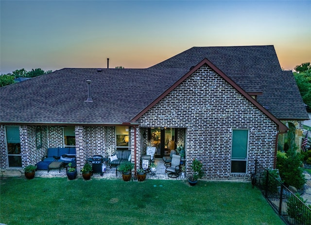 back house at dusk featuring a patio area, a lawn, and an outdoor hangout area