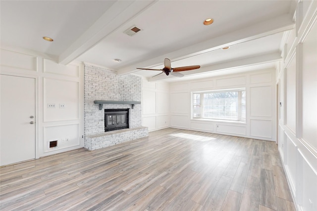 unfurnished living room featuring a brick fireplace, ceiling fan, beamed ceiling, and light wood-type flooring