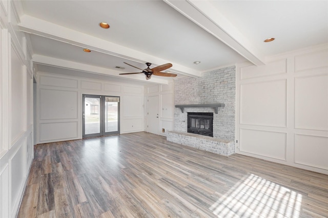 unfurnished living room with ceiling fan, a fireplace, hardwood / wood-style floors, and beamed ceiling