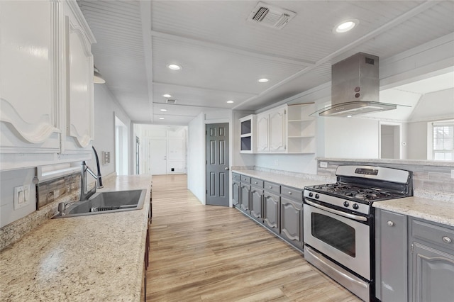 kitchen with island exhaust hood, white cabinetry, stainless steel range with gas cooktop, and sink