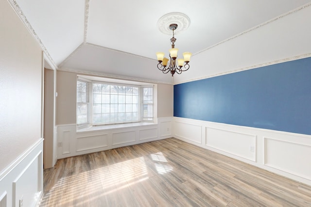 spare room with crown molding, wood-type flooring, vaulted ceiling, and an inviting chandelier