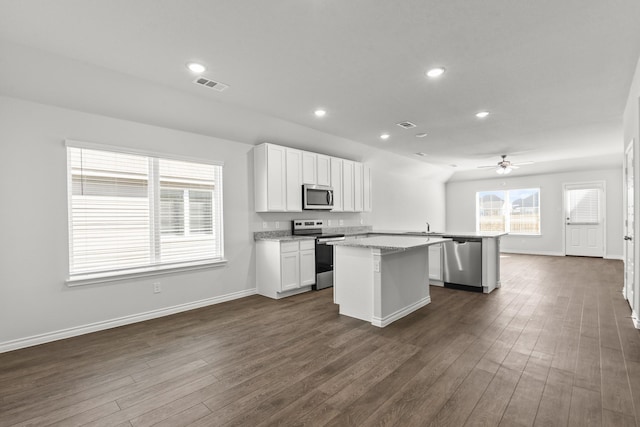 kitchen featuring white cabinets, appliances with stainless steel finishes, a center island, dark hardwood / wood-style floors, and light stone counters