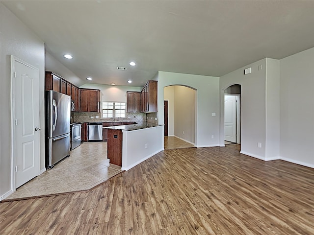 kitchen featuring tasteful backsplash, a kitchen island, sink, light hardwood / wood-style flooring, and appliances with stainless steel finishes