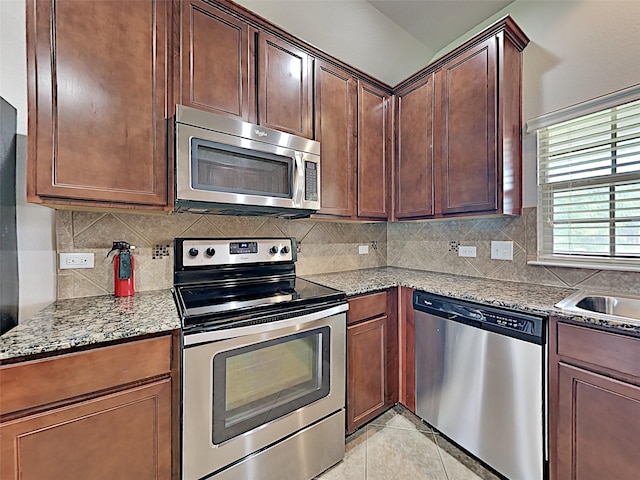 kitchen with light tile patterned flooring, appliances with stainless steel finishes, decorative backsplash, and light stone countertops