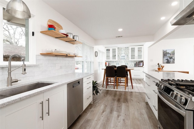 kitchen with light stone countertops, white cabinets, stainless steel appliances, light hardwood / wood-style floors, and sink