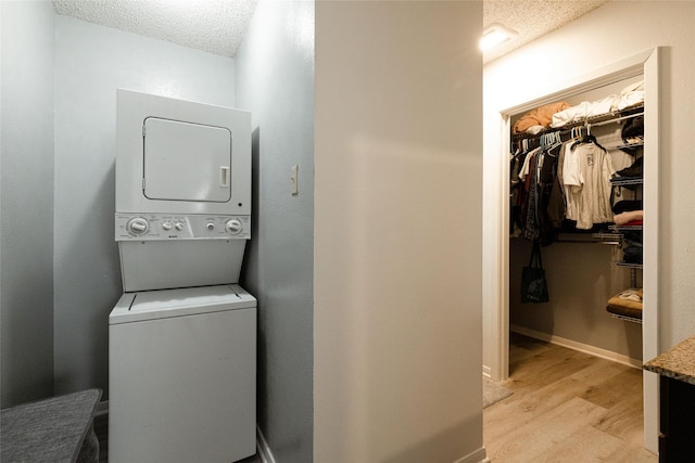 washroom featuring light wood-type flooring, stacked washer and dryer, and a textured ceiling